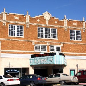 multistory brick building with light blue marquee "Lyric" and cars out front