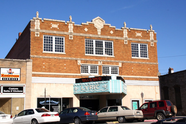 multistory brick building with light blue marquee "Lyric" and cars out front