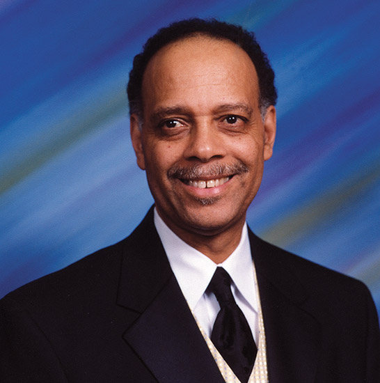 African-American man with mustache smiling in suit and tie