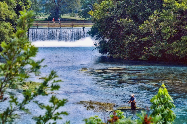 man fly fishing with waterfall and pedestrians in background