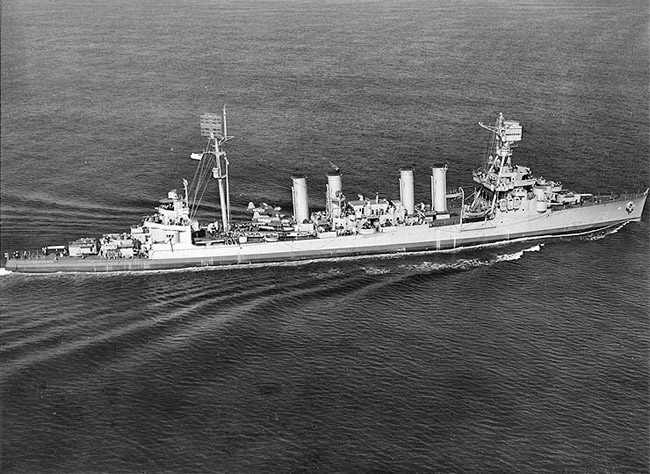 Aerial view of naval ship with four smokestacks underway at sea