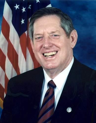 white man in suit and tie standing before American flag