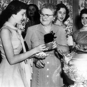several young white women surround punchbowl as older woman hands one woman a cup