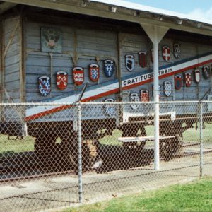 Train car with shields and striped banner under on display under car port with fence