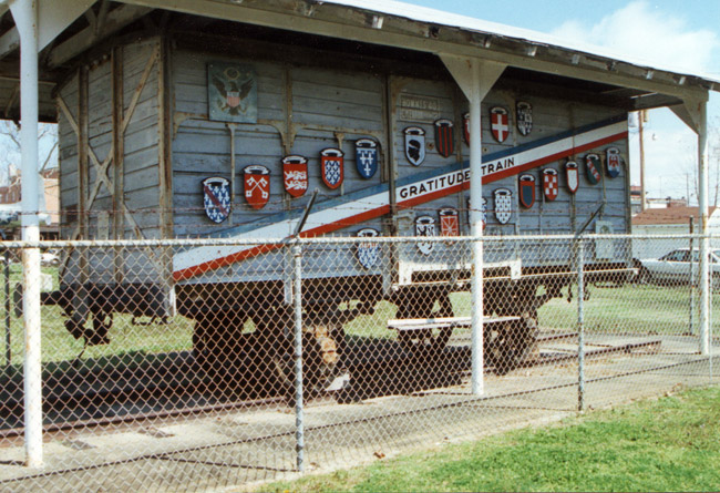 Train car with shields and striped banner under on display under car port with fence