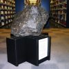 Meteorite on display including didactic text in library with bookshelves in background.