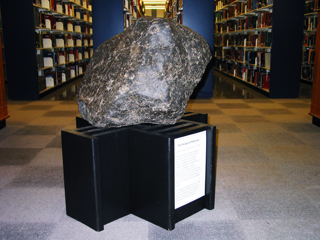 Meteorite on display including didactic text in library with bookshelves in background.