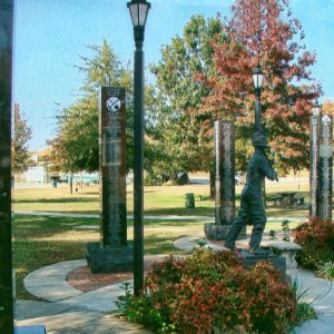 Statue of man with pick ax surrounded by engraved columns on walking path in park with lamps and trees in the background