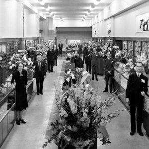 Dressed up department store workers pose in aisles by glass cases racks displays flower bouquets