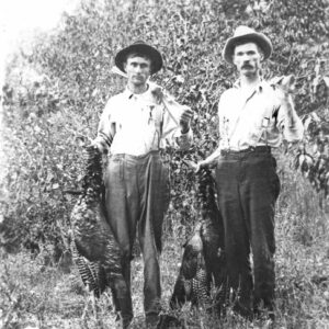 Two white men in overalls and hats posing with recently killed turkeys