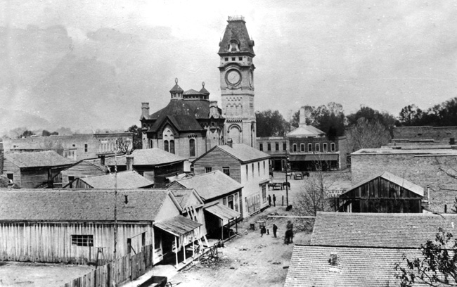 Street scene featuring  wood framed houses and downtown brick architecture and large clock towner in background