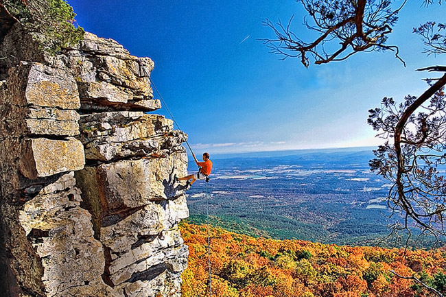 man climbing striated rock face overlooking fall trees