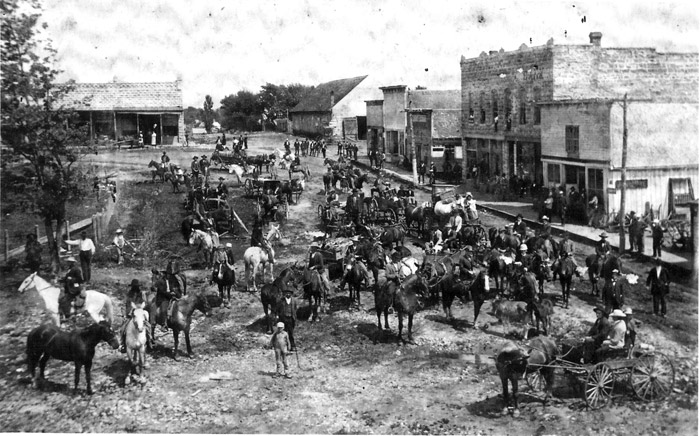 Numerous horses with riders in street with buildings in background