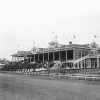 Horses on track running by crowded stands and main buildings