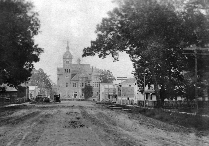 tree-lined wide dirt road leading to multistory building with steeples and clock tower
