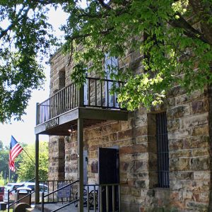 Two-story stone building with balcony and barred windows, American flag