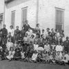 White students and teachers posing for a group photo outside single-story school house