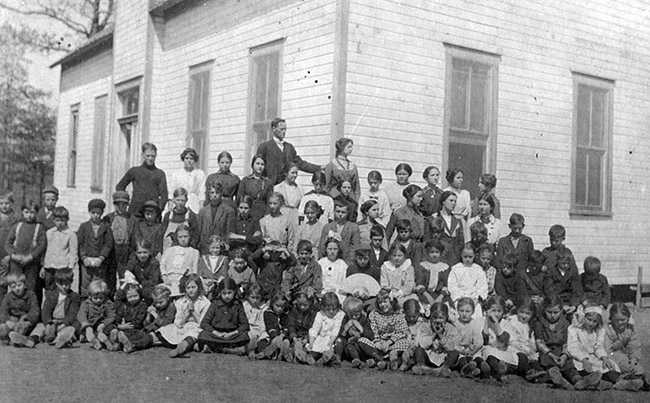 White students and teachers posing for a group photo outside single-story school house