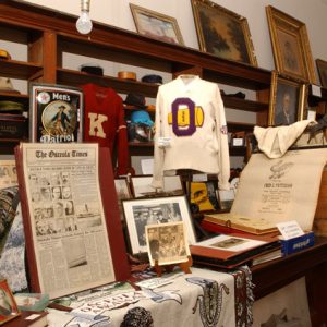 Framed photographs newspapers and sports memorabilia on display in room with tables and wooden shelving