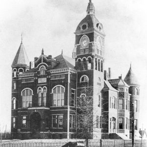 Multiple-story courthouse with clock tower and arched entrance surrounded by an iron fence