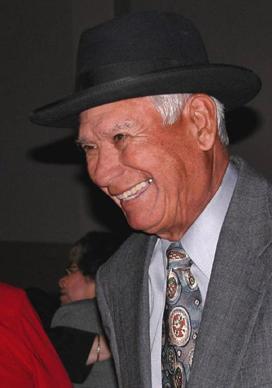 Native American man with short gray hair smiling in hat and suit