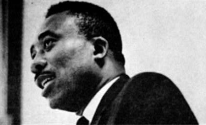 profile view of black man speaking with short hair and mustache wearing a suit and tie