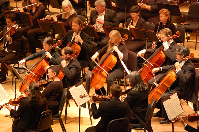 White men and women dressed in black sitting in rows of chairs playing classical instruments