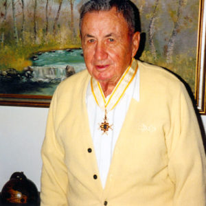 Old white man wearing a medal with painting on the wall behind him