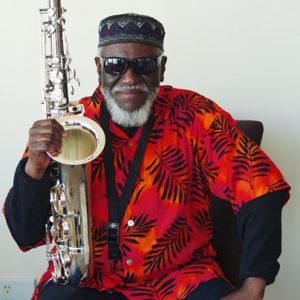 African American man dressed in colorful shirt, sunglasses, and cap holding saxophone