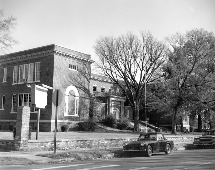 Two-story brick building with trees and parked cars