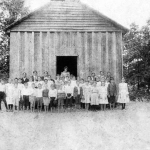 Group portrait white school children with teachers outside wood-frame gabled building