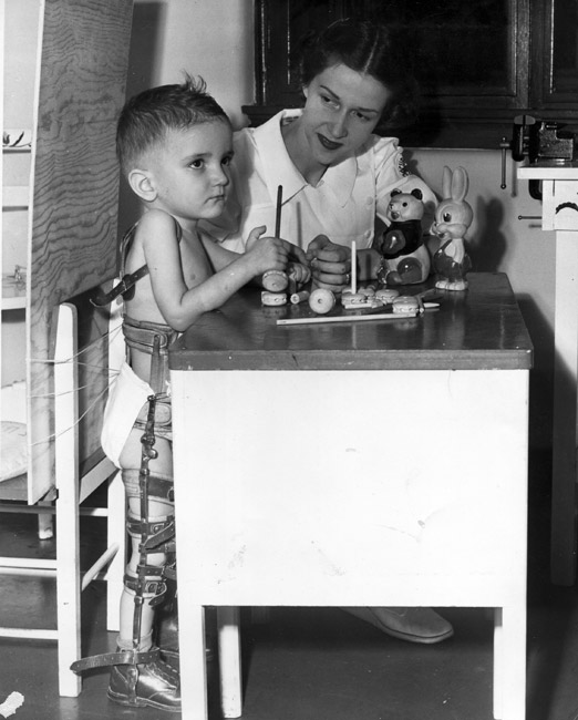 White boy in body brace and white woman playing with toys at small table