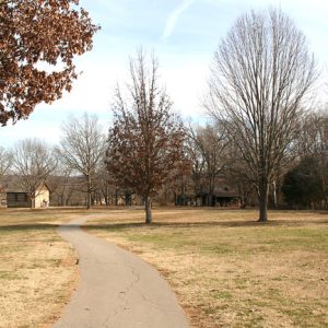 paved trail through field with trees and small buildings