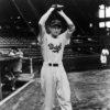 White male baseball player "Dodgers" uniform poses arms glove raised few players spectators watching