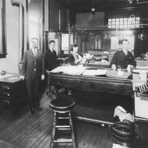 White men in suits and white woman working at a bank