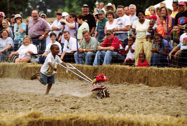 Black boy Smiling and running with small tiller on dirt track with  audience watching