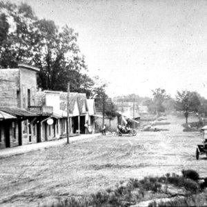 Street scene with wooden buildings and cars on a dirt road