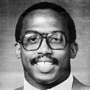 Portrait of a black man in a suit, tie, and glasses.