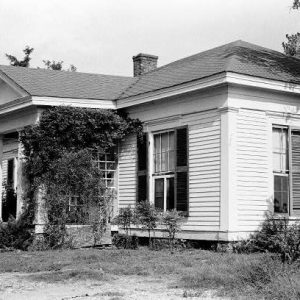 Side view of single-story house with vines growing on side of covered porch and white siding