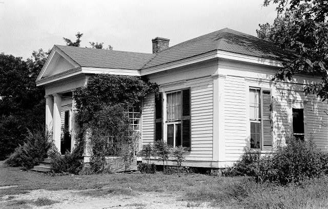 Side view of single-story house with vines growing on side of covered porch and white siding