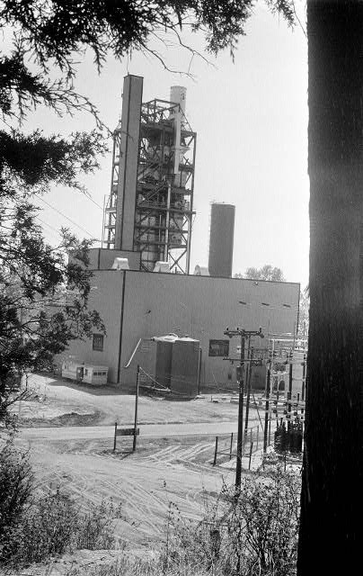 Industrial building with tall steel stairwell structure and power substation with foreground trees