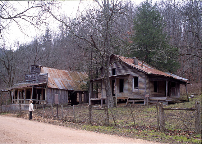 Abandoned wooden house and store on dirt road with fence