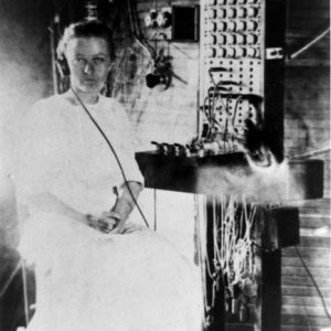 Young stern white woman seated with hands crossed posing by switchboard wearing headphones