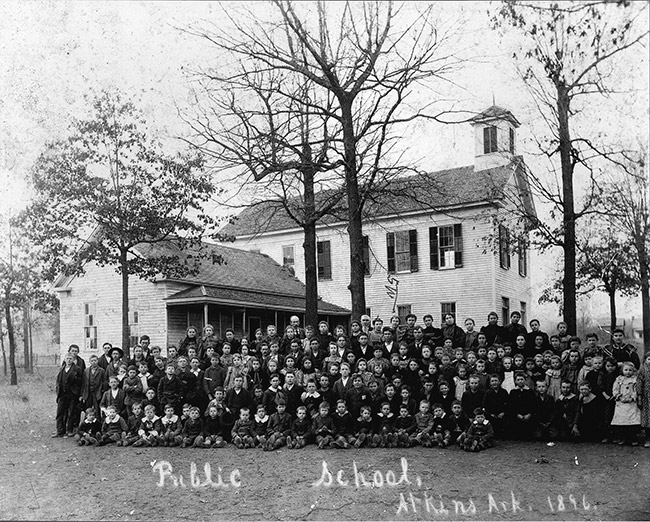 large group of white children and faculty posing together with multistory building with cupola and house in the background