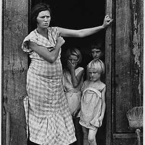 Mother in dress shoes and three shoeless girls leaning in wood frame house doorway