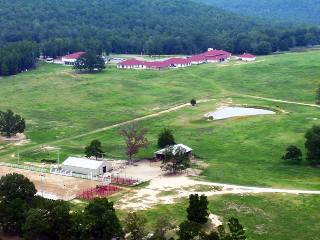 Aerial view of a large field among mountains with building complex opposite barns corral and pond