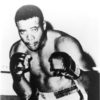 Portrait African-American male boxer with gloves raised, shorts, boots, in corner of ring