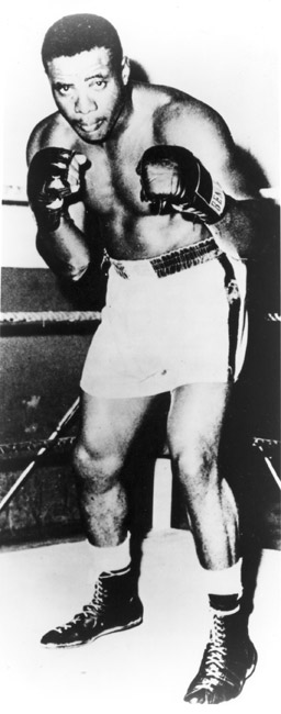 Portrait African-American male boxer with gloves raised, shorts, boots, in corner of ring