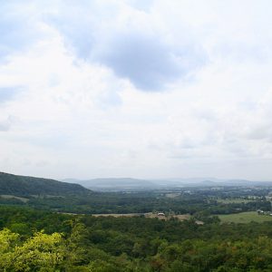 View looking over tree covered countryside with farmland and mountains in the background