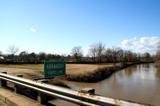 sign next to river "Arkansas State Line"